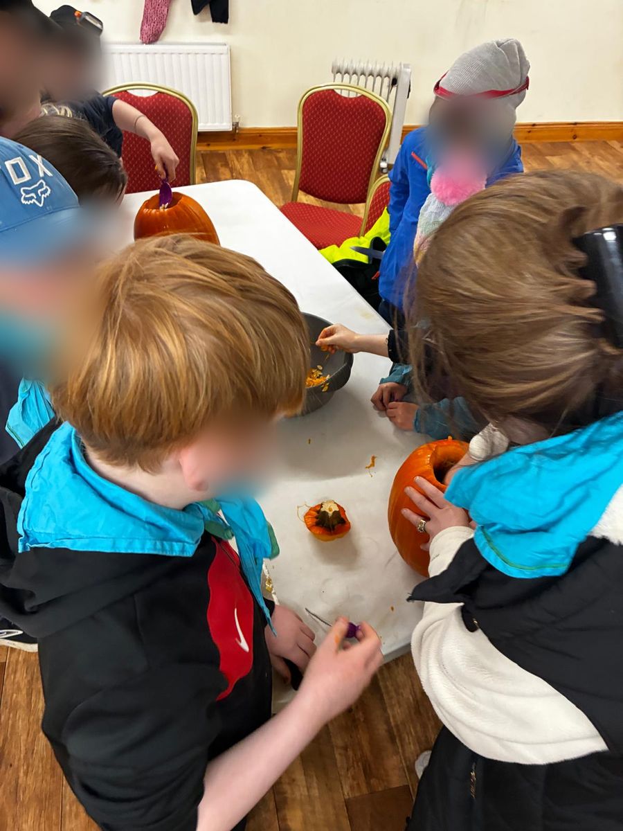 Cubs in their neckers gathered round a table carving pumpkins (faces blurred)