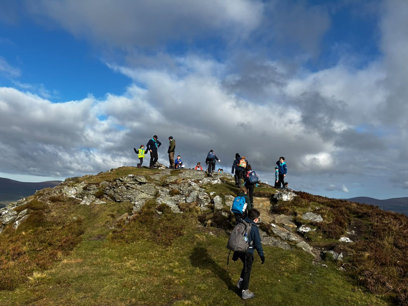 Cubs and leaders reaching the rocky summit of Scarr on a sunny autumn day, with one Cub walking up in the foreground